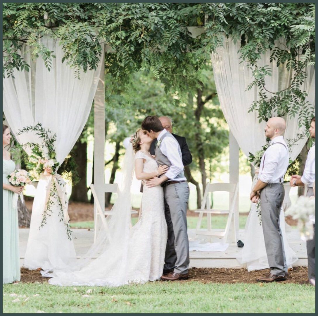 A couple kissing under an arbor at their wedding.